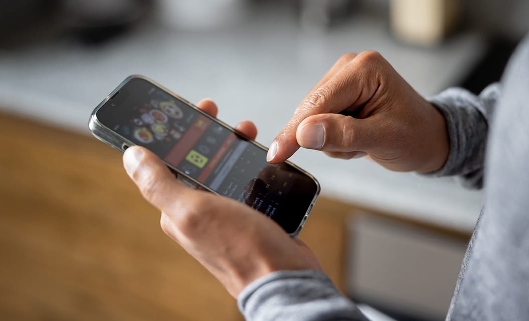 Närbild på en persons händer där denne håller i en smartphone och spelar på en bettingsajt.