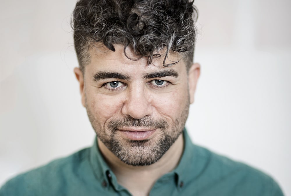 Socionomen och författaren Zhiwar Rashid tittar rakt mot kameran, huvud och axlar syns, ståendes framför en ljusgrå bakgrund.