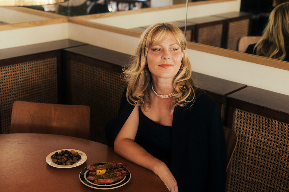 Författaren Elina Pahnke sitter finklädd i klänning på en fin restaurang, vid ett bord där två tallrikar mat står uppdukade.