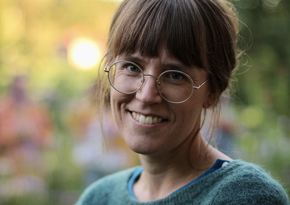 Porträtt på Lovisa Hanberger, huvud och axlar, framför en ofokuserad bakgrund av grönska.