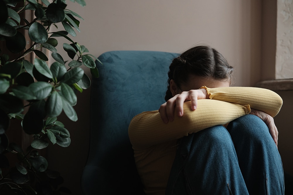 En anonymiserad ung tjej sitter med huvudet lutad mot korsade armar som vilar mot knäna, tillsynes ledsen och trött.
