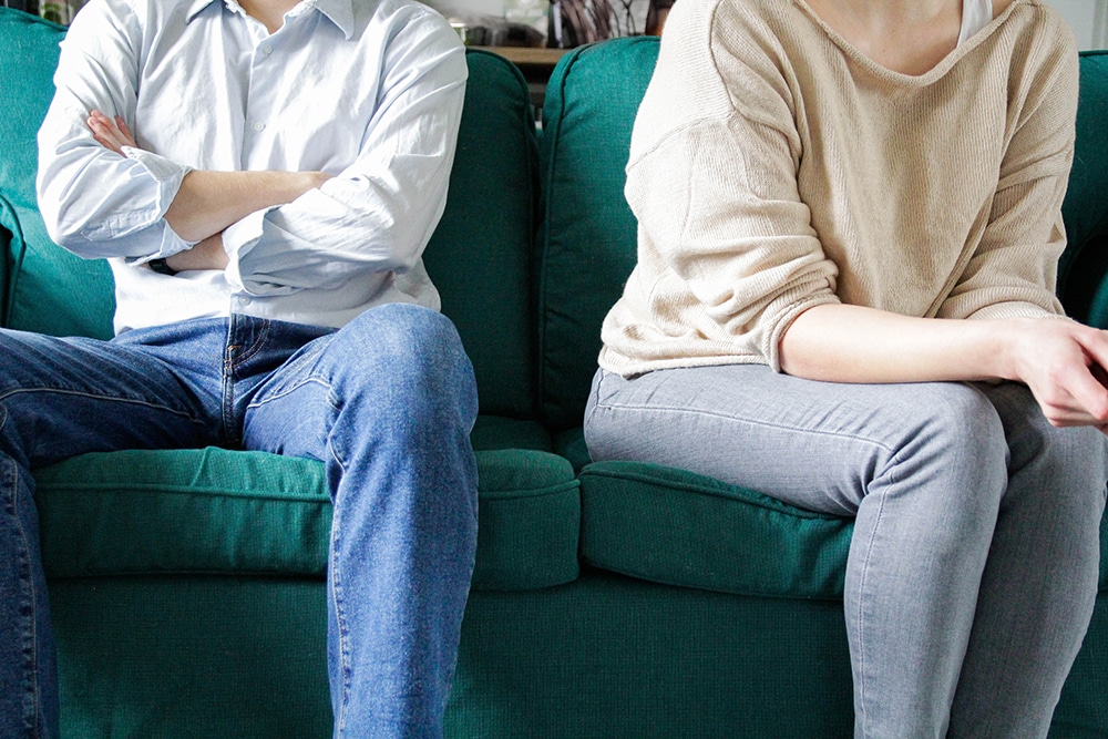 Två personer vars ansikten inte syns sitter i en soffa, den ena med armarna i kors, den andra vänd bort från personen bredvid.