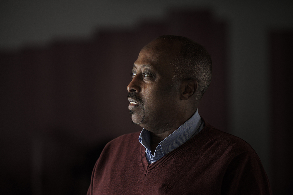 Närbild på Yusuf Abdow, huvud och axlar, med blicken vänd åt vänster, svagt upplyst inne i Örebro moské.