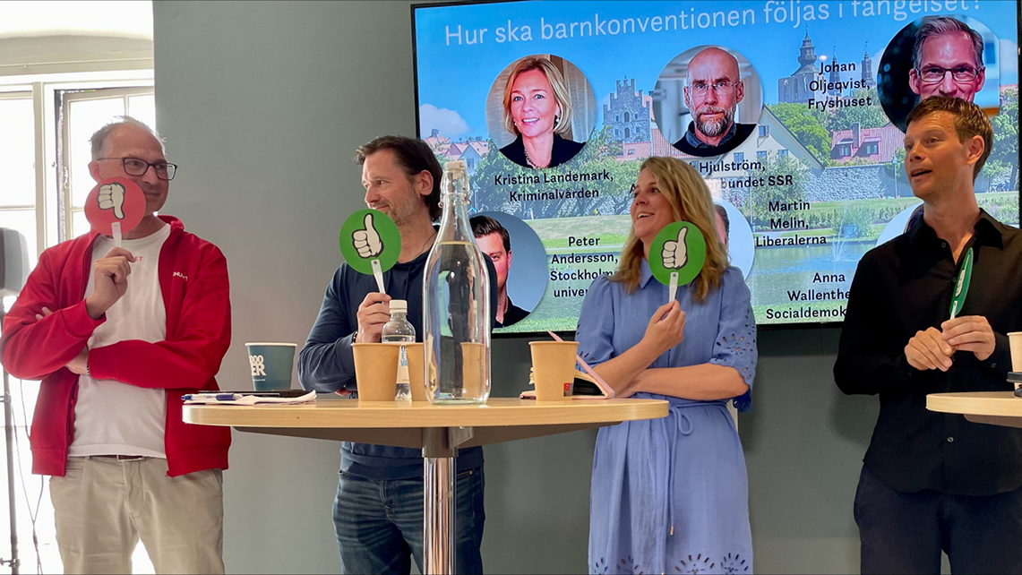 Paneldebatt: Fyra personer står vid ett bord för paneldiskussion och håller gröna tummen upp-skyltar