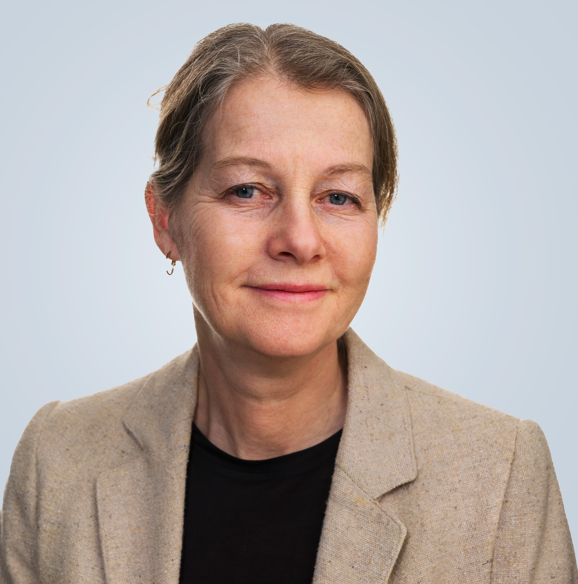 Porträttbild på Annika Clemens med ljust hår iklädd en beige kavaj och svart tröja. Tittar in i kameran och ler.