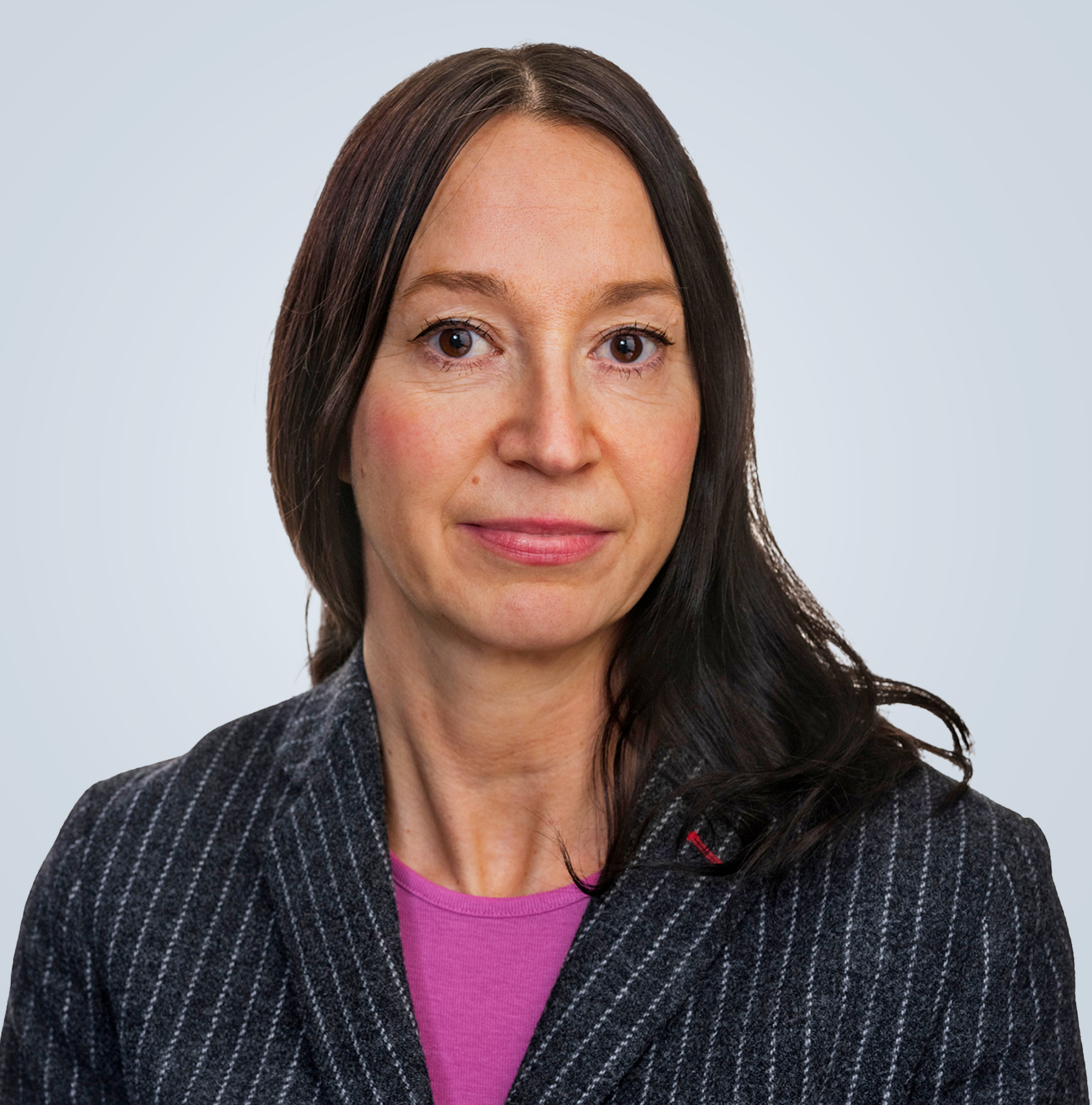 Porträttbild på Therese Johansson med mörkt hår iklädd en mörkgrå kavaj med vita ränder och rosa tröja. Tittar in i kameran och ler.