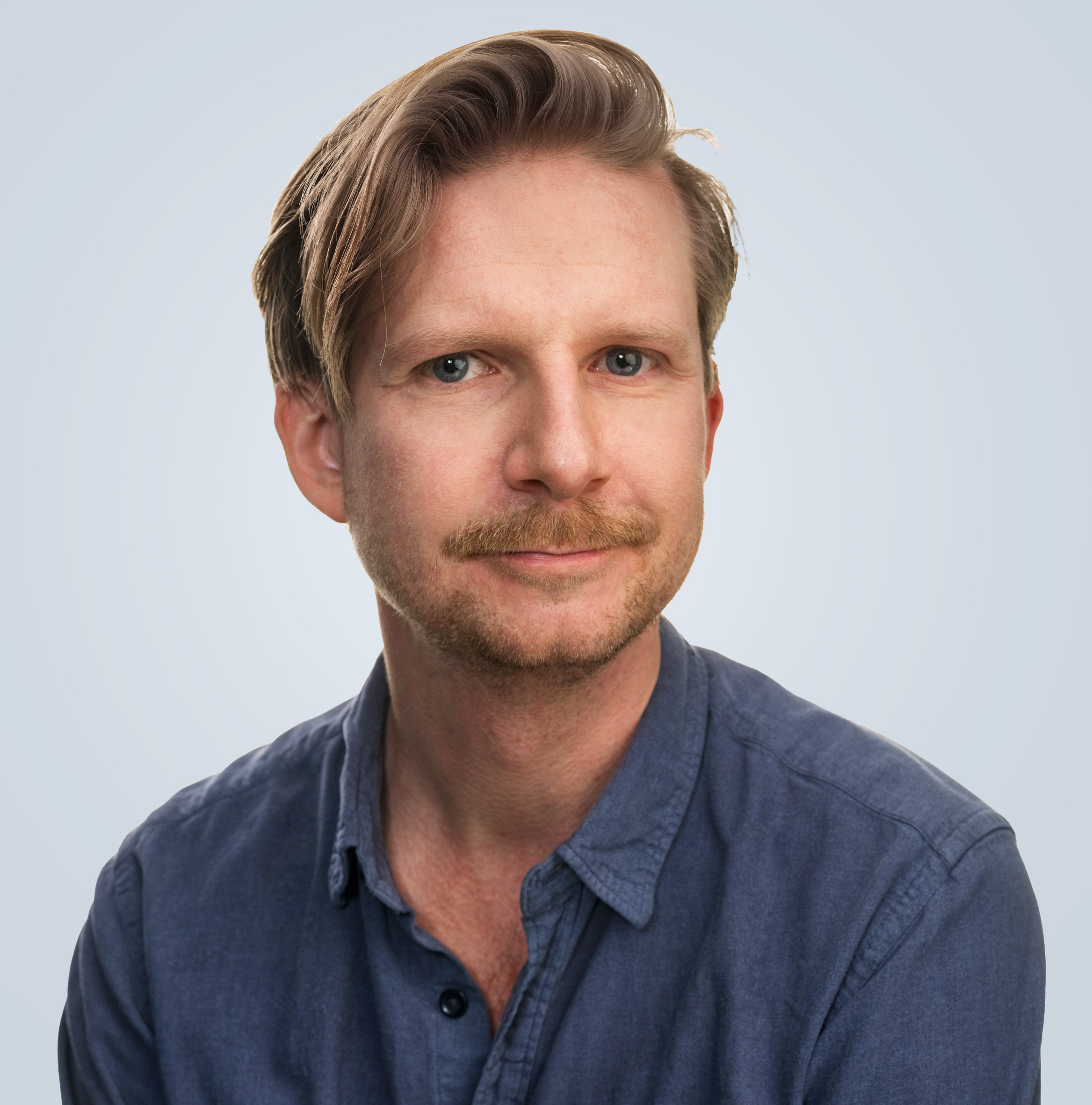Porträtt på Tim Andersson i blond kort hål, mustache och blå jeans skjorta.