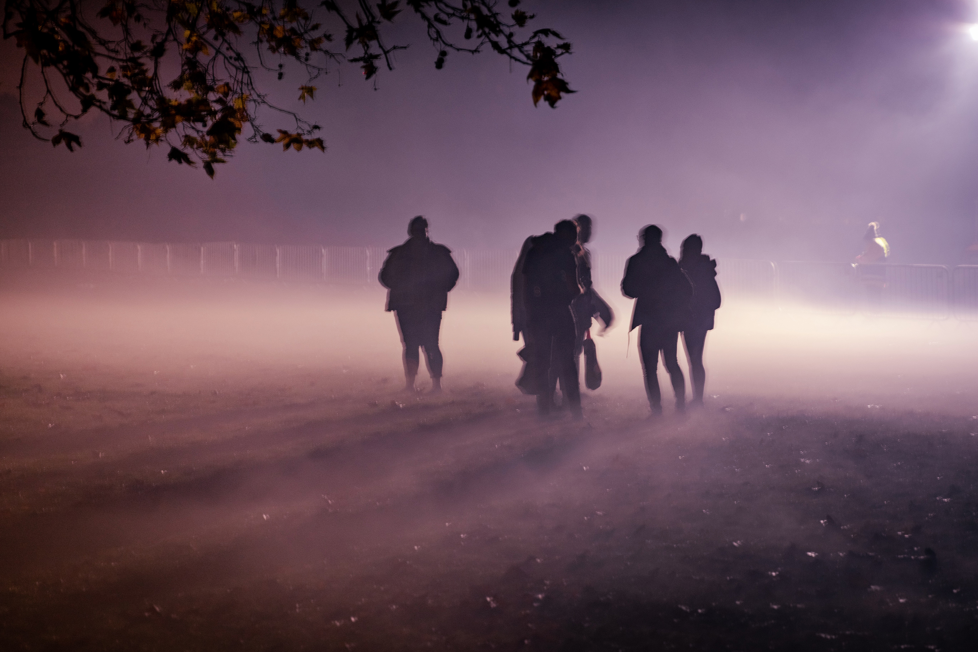 En grupp personer går genom ett utomhusområde på natten, där deras skuggor syns tydligt på marken.