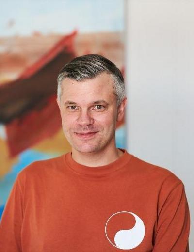 Tobias Davidsson med kort grått hår bär en orange tröja med ett vitt cirkelformat mönster och står framför en suddig bakgrund.