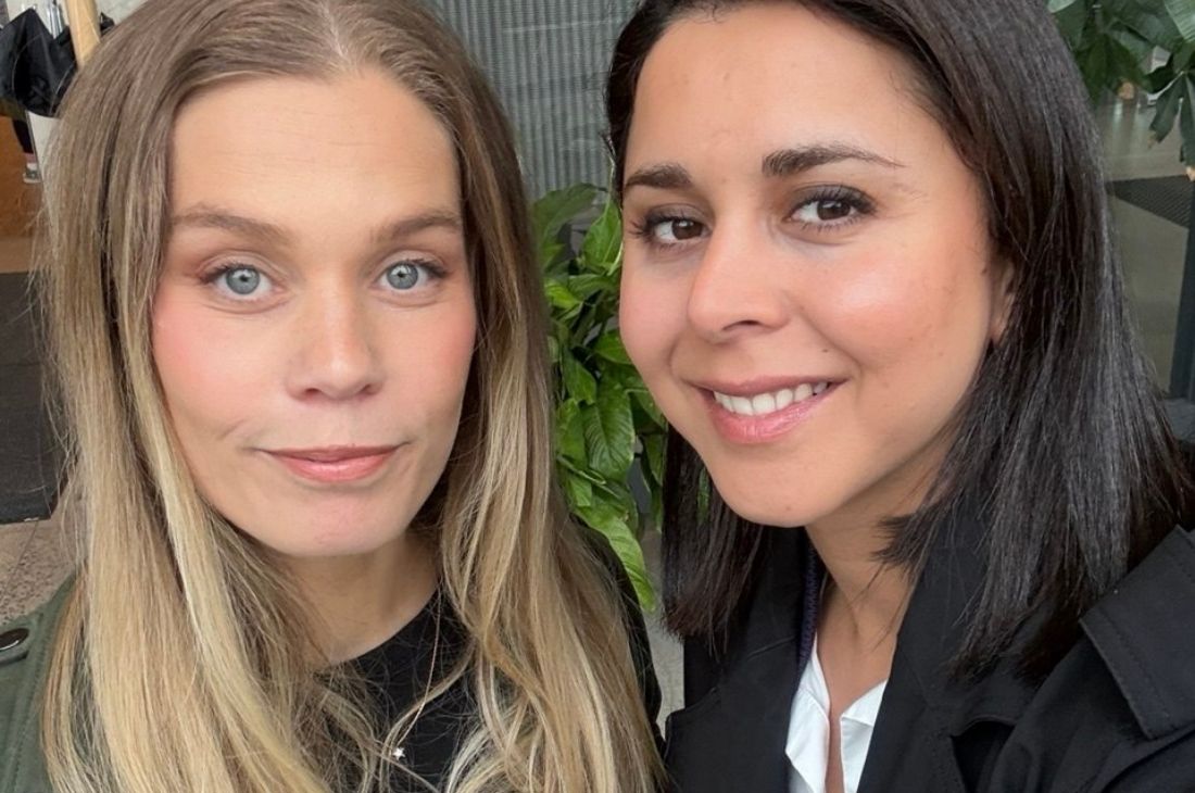 Nora Talts Ellertsen och Parirokh Motamed Ardameh. står nära varandra inomhus och tittar mot kameran med ett svagt leende. I bakgrunden syns en grön växt och en del av en byggnadsentré.