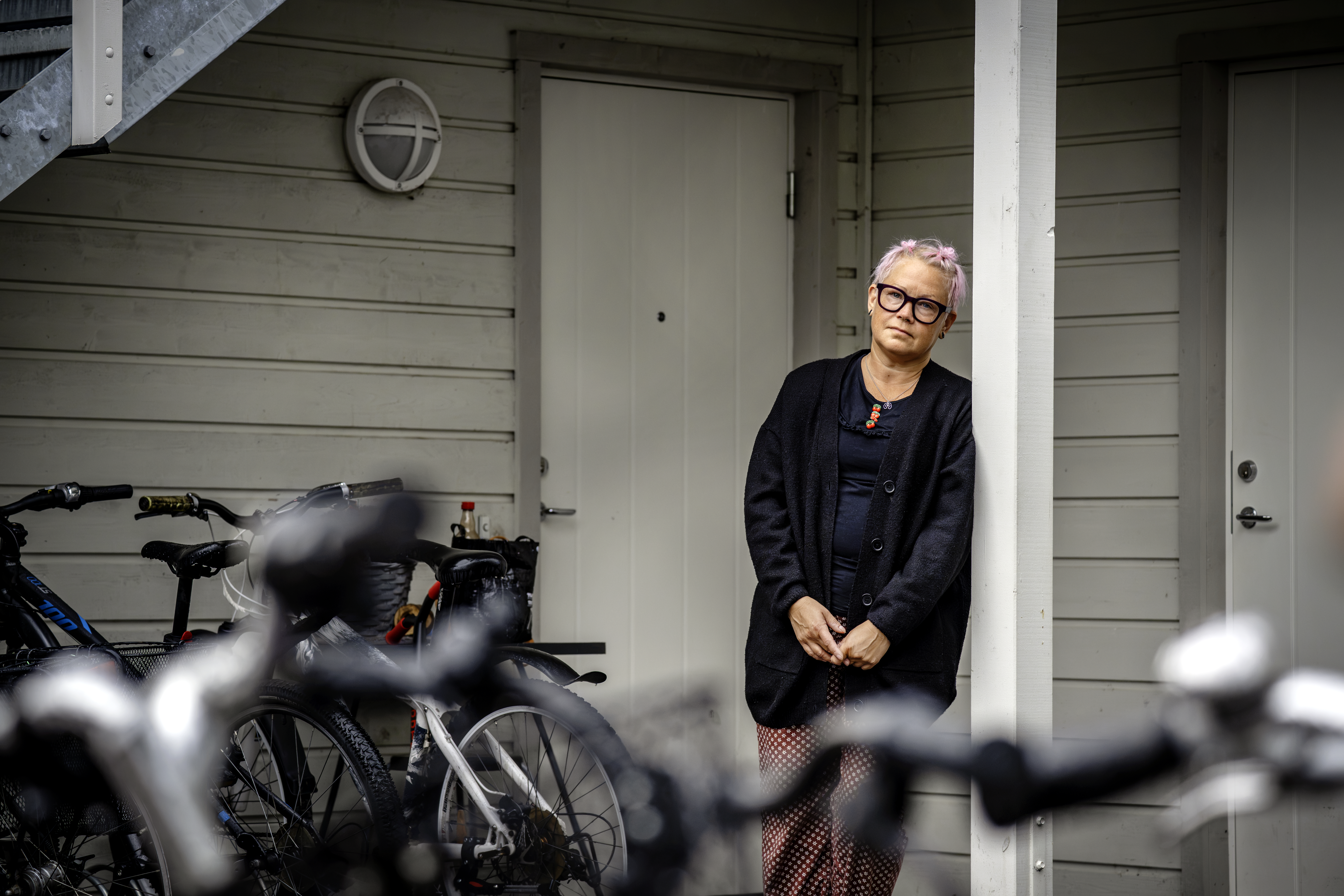 Marie Gustafsson med glasögon och ljust hår står vid en stolpe utanför en byggnad, med flera cyklar parkerade i närheten.