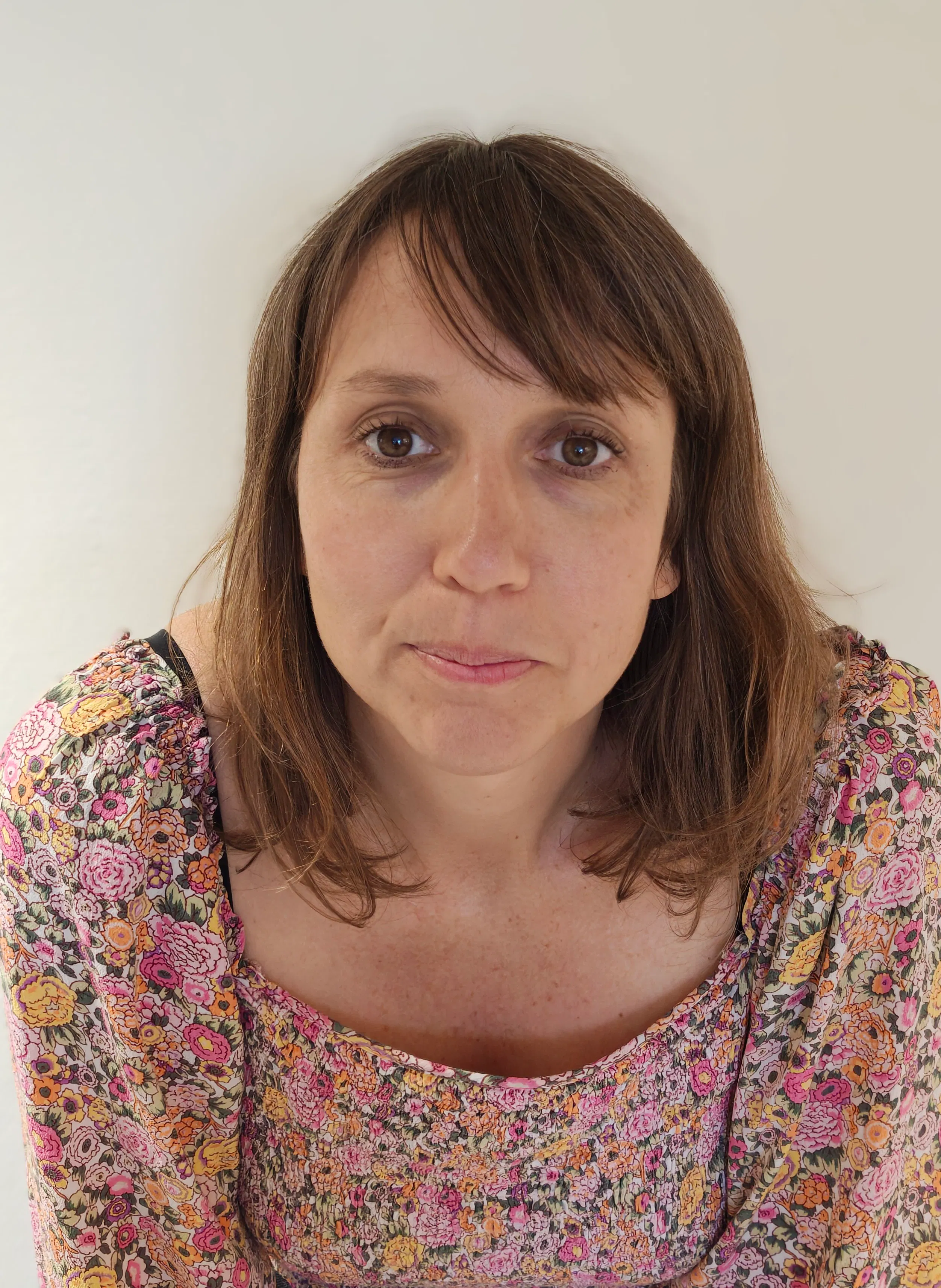 Jenny Langguth med rakt brunt hår och en blommig topp tittar rakt in i kameran mot en ljus bakgrund.