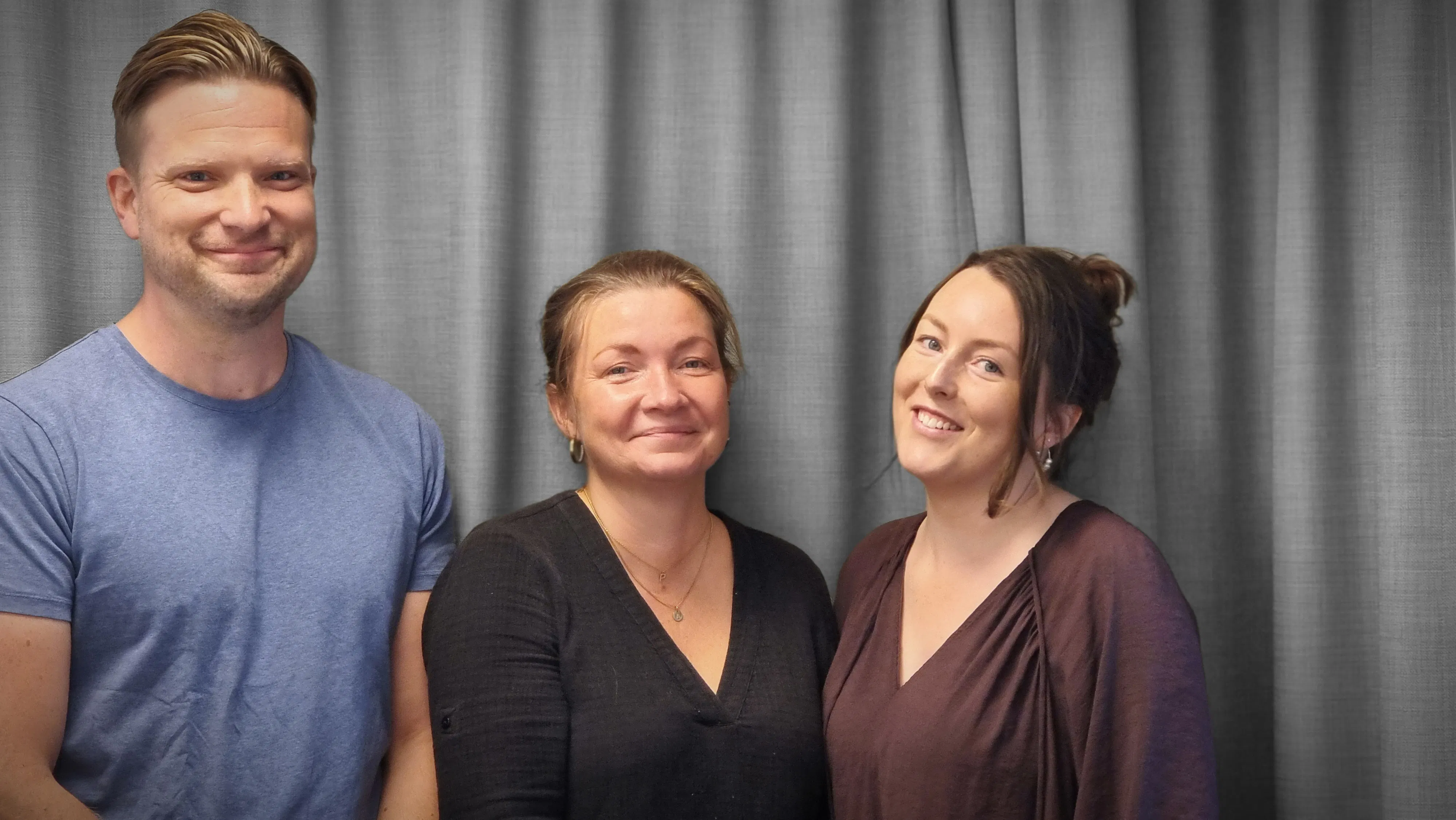 Fredrik Nygren, Lina Bolund och Sofia Groth står framför en grå gardin och tittar in i kameran.
