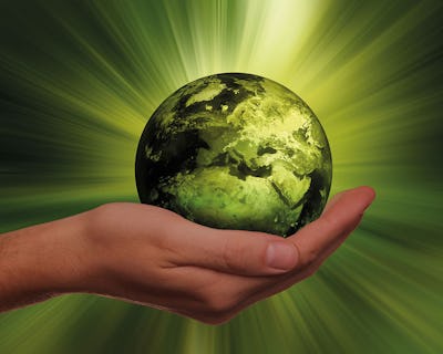 En hand håller i en grön planeten Jorden.