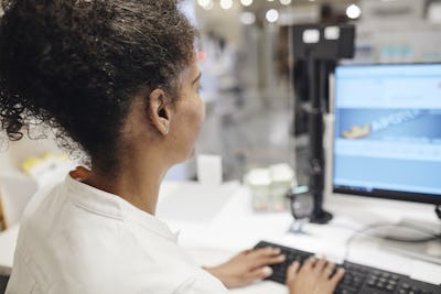 Kvinna sitter framför datorn i ett apotek.