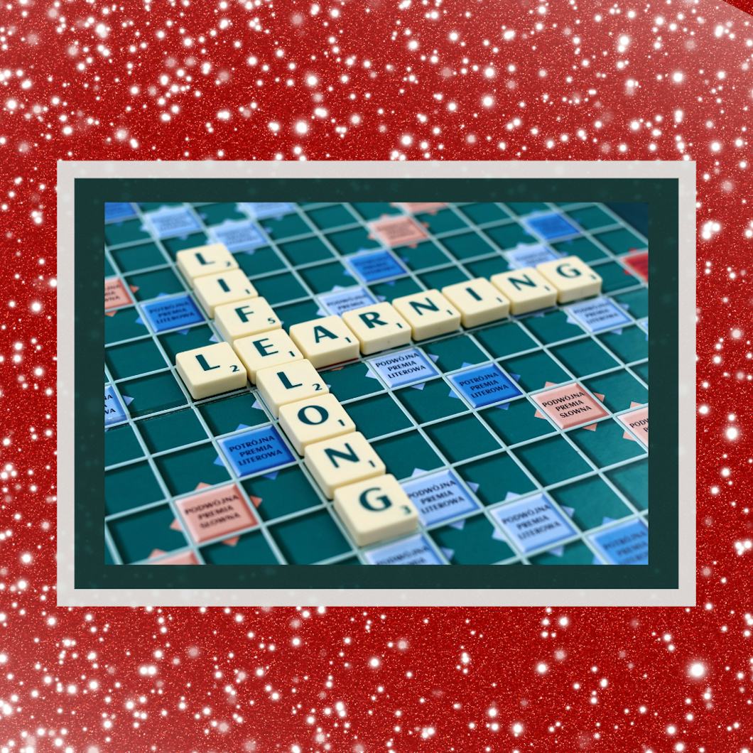 Scrabblebrickor bildar orden "Lifelong Learning" på ett korsordsvis på en bräda, omringade av en röd och vit kant.