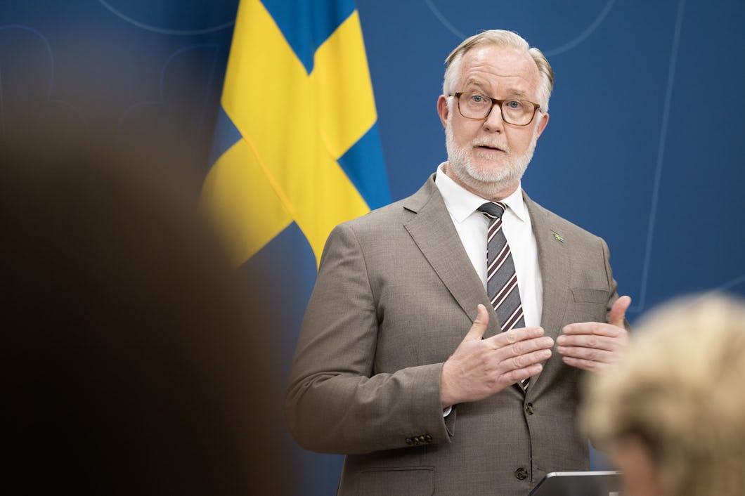 Utbildningsminister Johan Pehrson talar vid ett podium med en svensk flagga i bakgrunden.