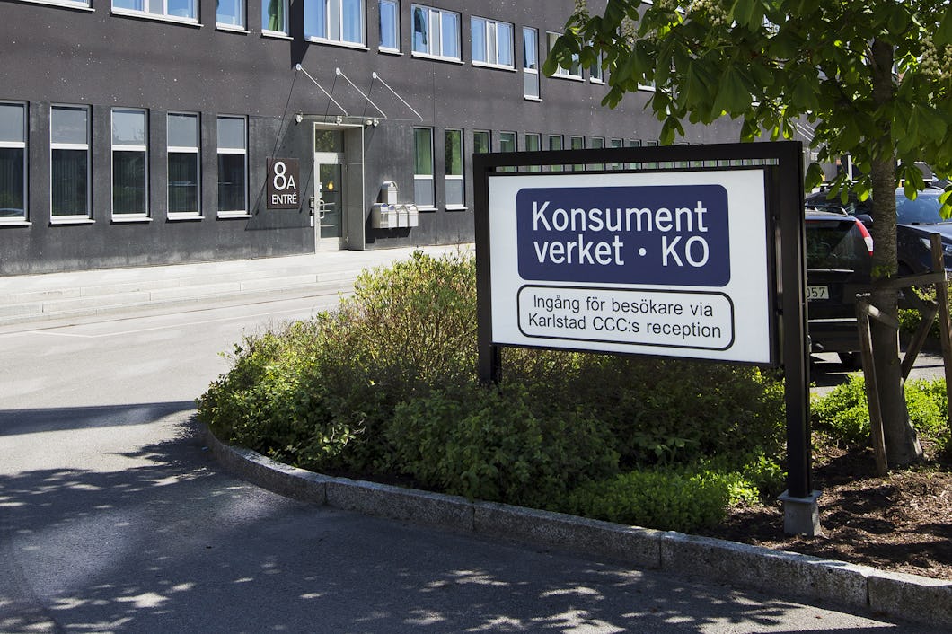 En skylt för Konsumentverket KO, omgiven av grönska, står utanför ett kontorshus.