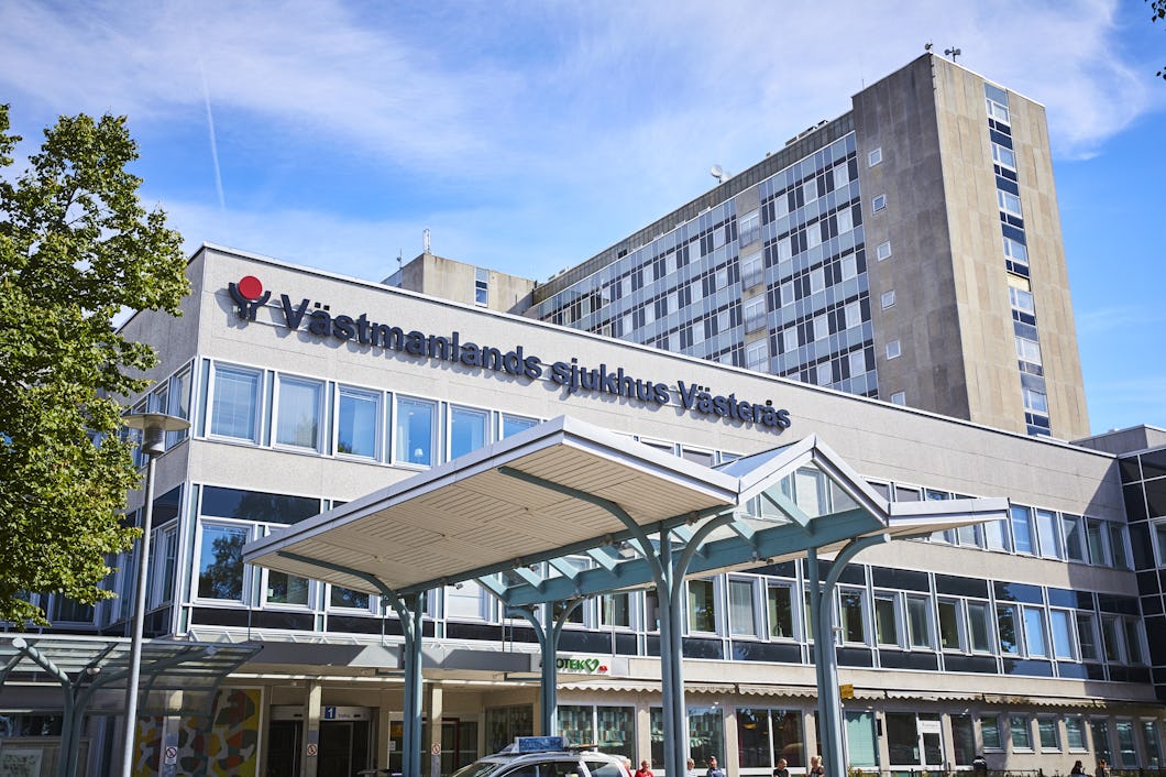 Ett sjukhus med skylten "Västmanlands sjukhus Västerås" på fasaden syns. En överbyggd entré finns i förgrunden.
