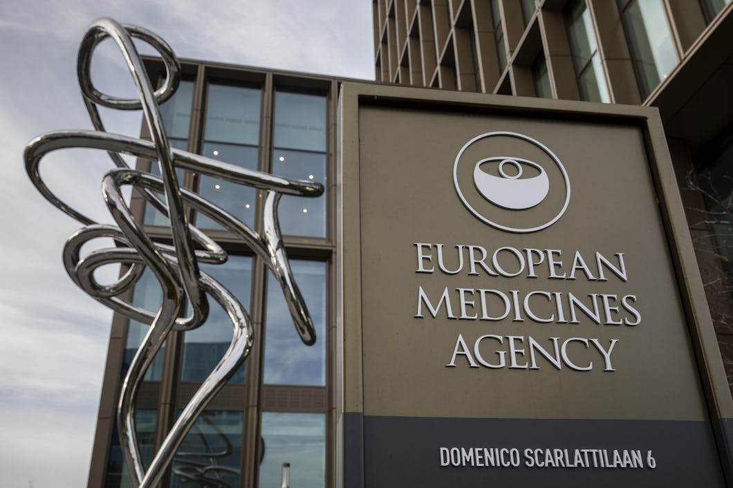Skylt för Europeiska läkemedelsmyndigheten med dess logotyp, en skulptur och en del av kontorsbyggnaden synliga i bakgrunden.
