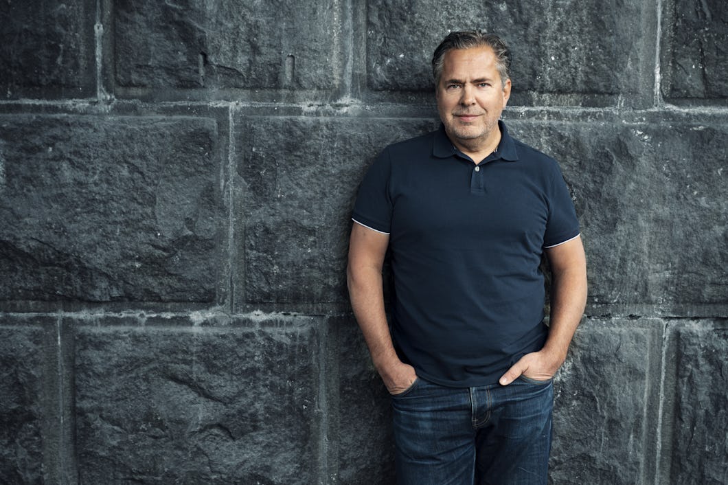 Pär Svärdson i en mörkblå pikétröja och jeans står med händerna i fickorna mot en stenmur.