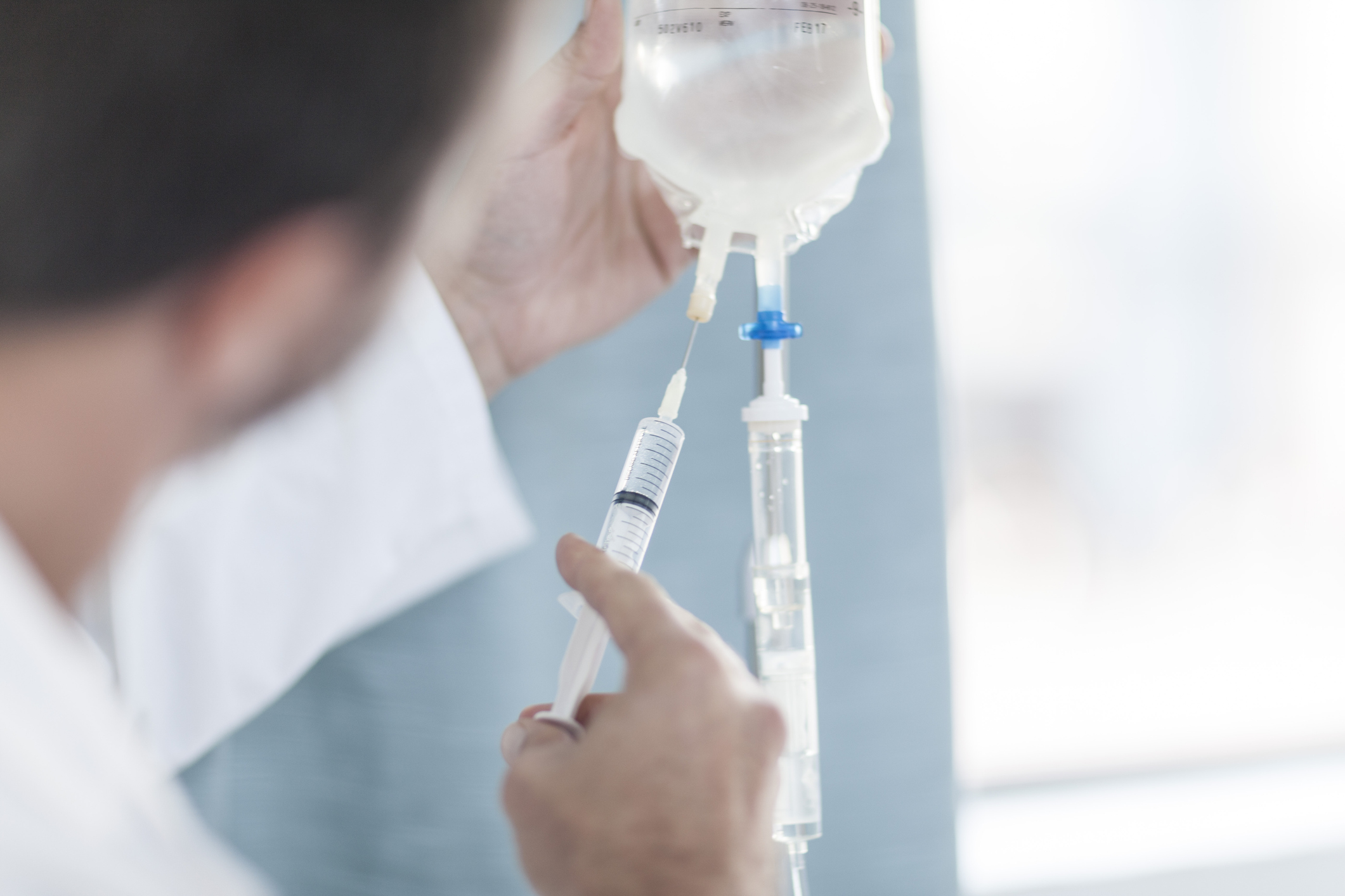 En person förbereder ett intravenöst dropp genom att injicera vätska från en spruta i en droppåse.