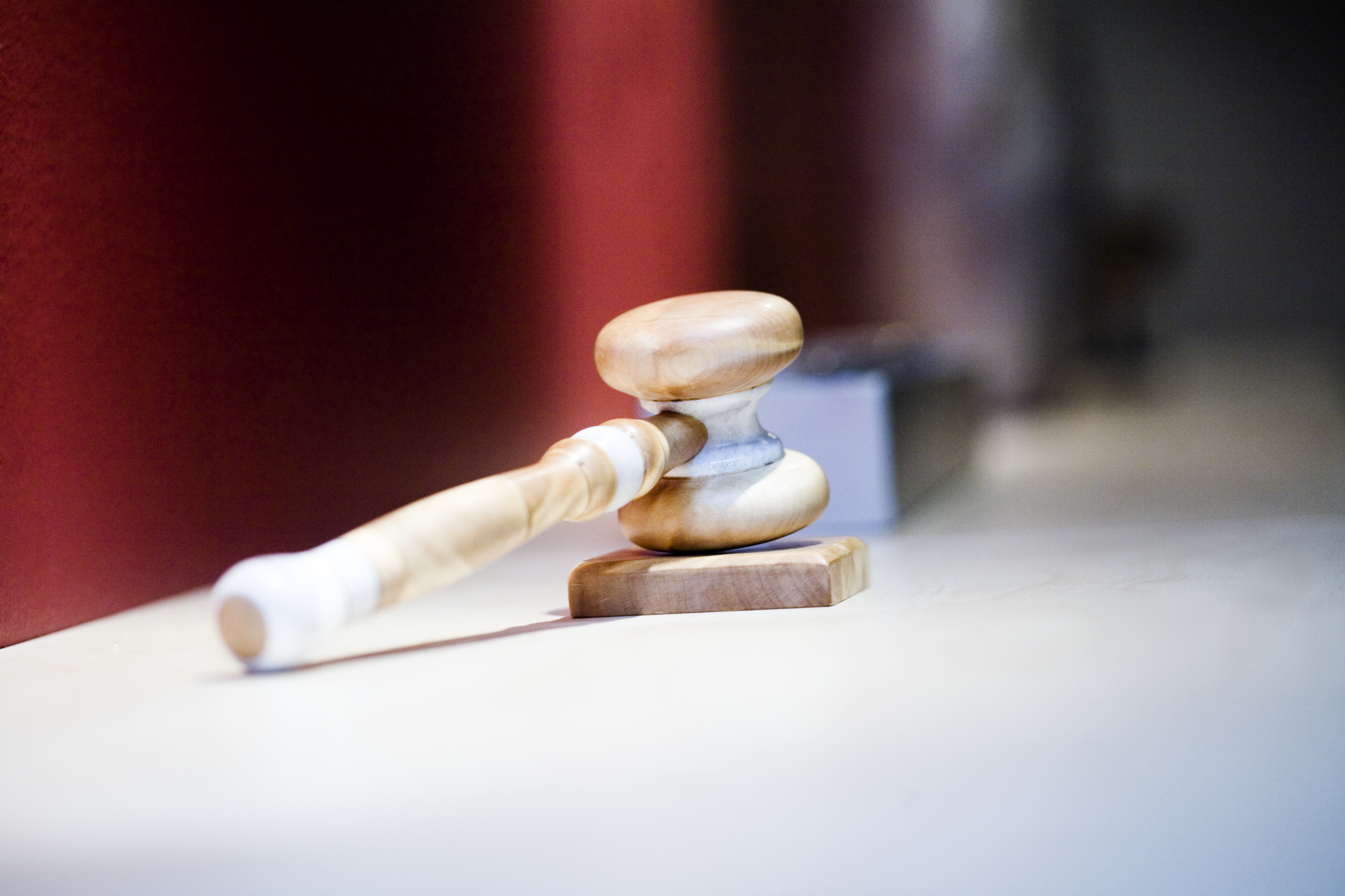 En träklubba ligger på sin ljudplatta på en ljus yta med en suddig röd bakgrund.