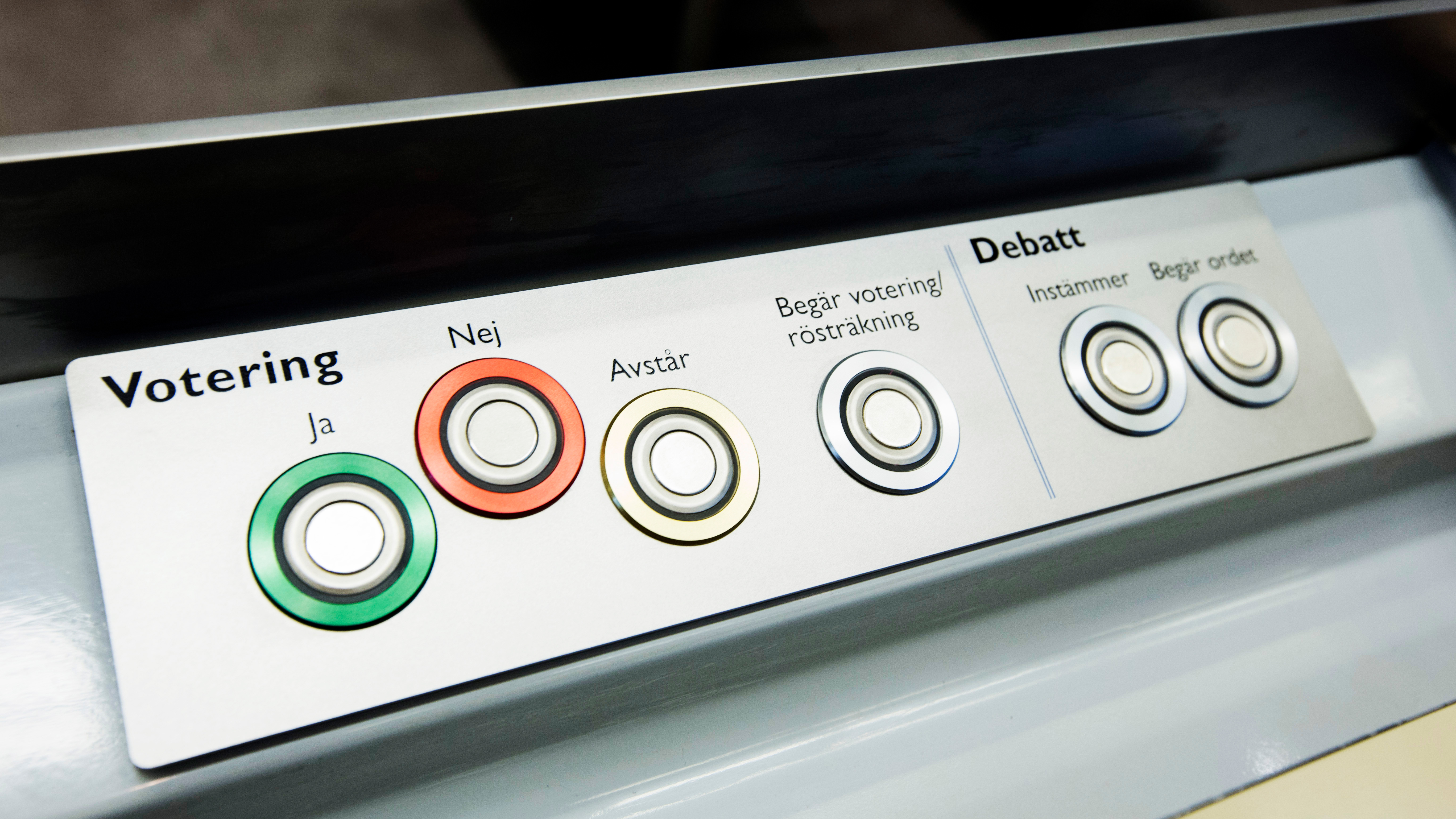 Voteringsknappar i en ledamotsbänk; grön knapp för "ja", röd "nej" och gul "avstår".