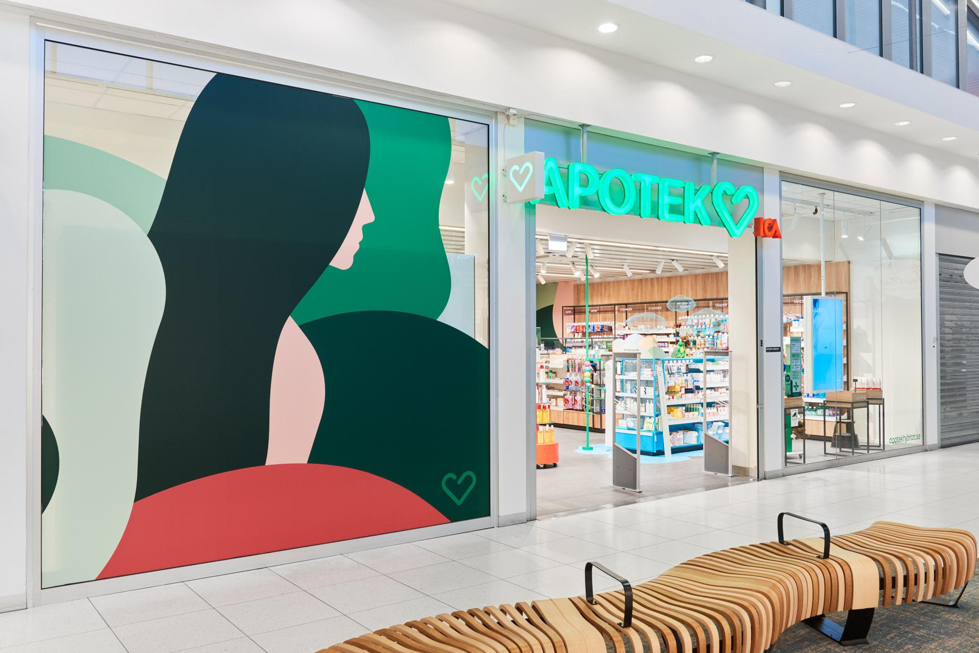 Ett apotek med neonskylten "APOTEK"; på fasaden finns en stor målning av en kvinna med långt mörkt hår.