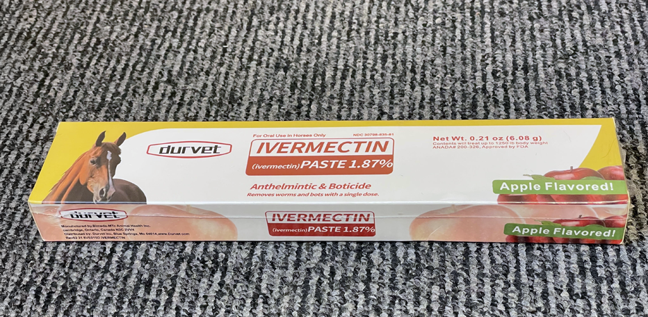 En ask Durvet Ivermectin Paste 1,87% för hästar, äppelsmak, märkt som avmaskningsmedel och botmedel på grå matta.