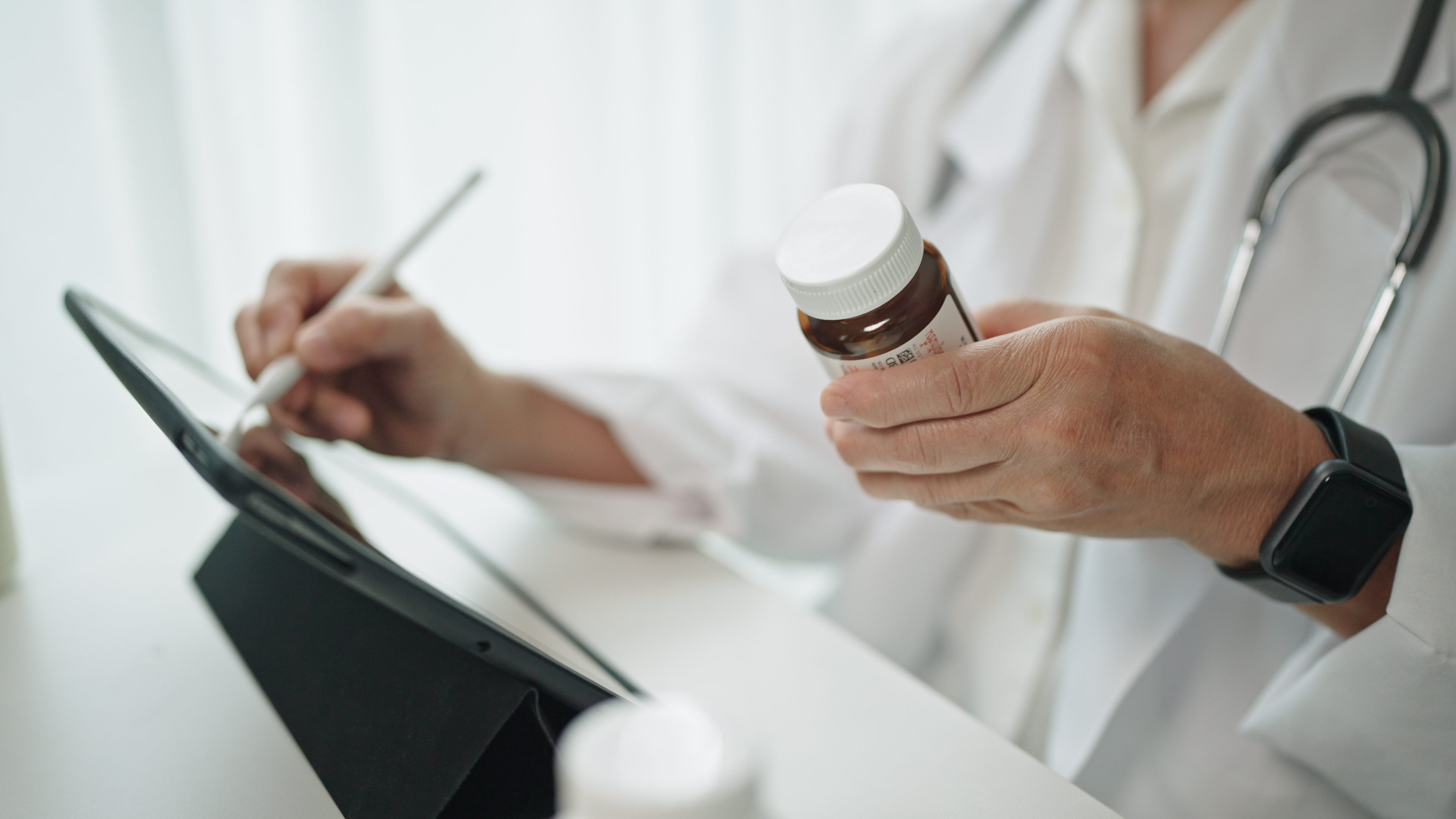 En läkare håller en pillerburk i ena handen och skriver på en surfplatta med en stylus i den andra handen.