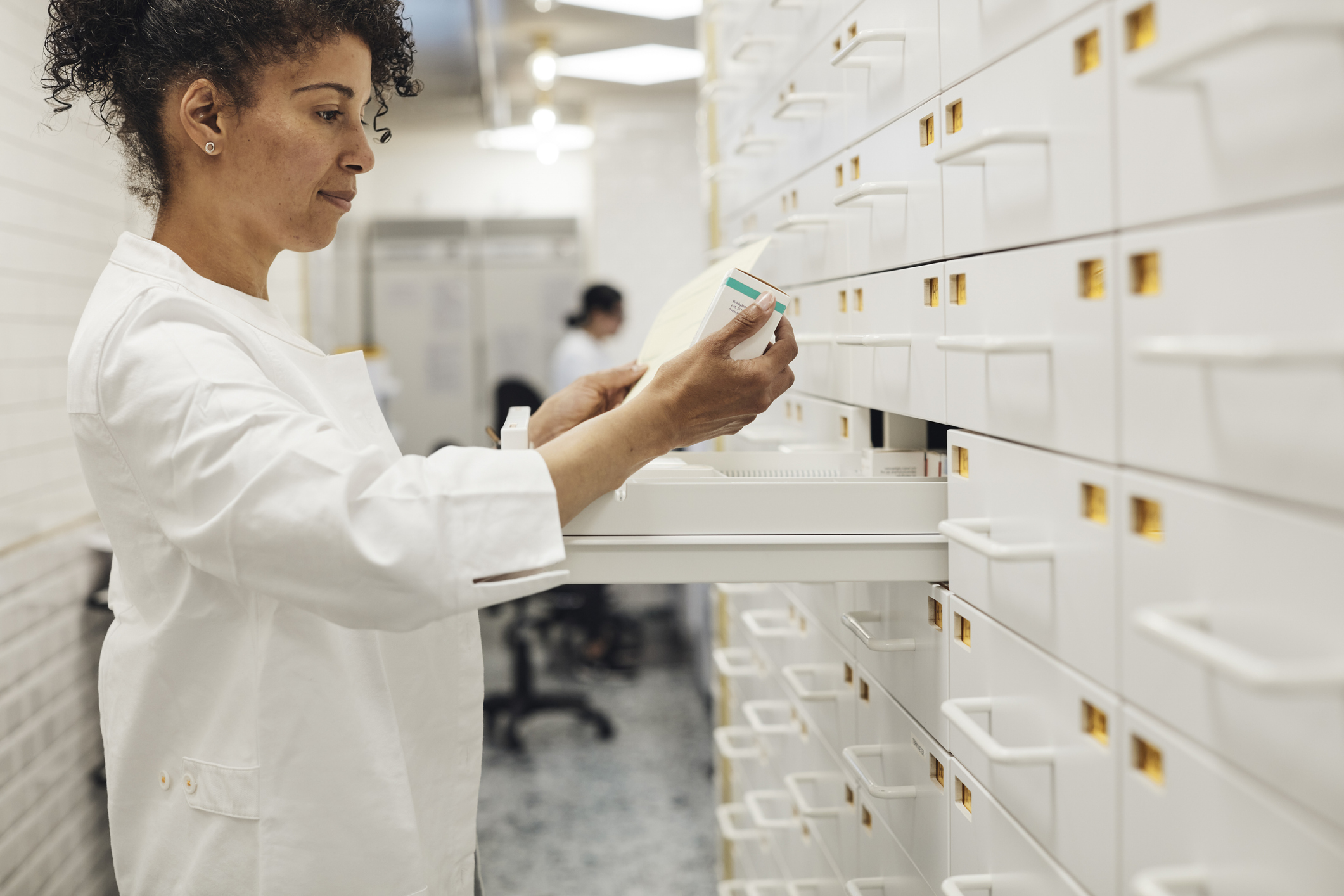 En farmaceut i vit rock tar medicin ur en låda i ett apotek med förvaringsutrymmen.