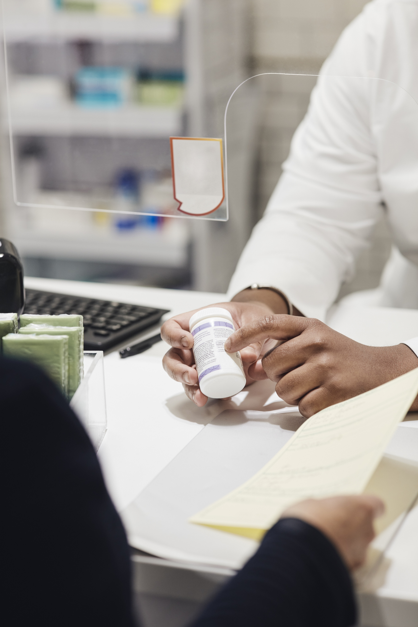 En farmaceut förklarar läkemedelsinstruktioner för en kund och håller en medicinburk, kunden håller ett papper över disken.