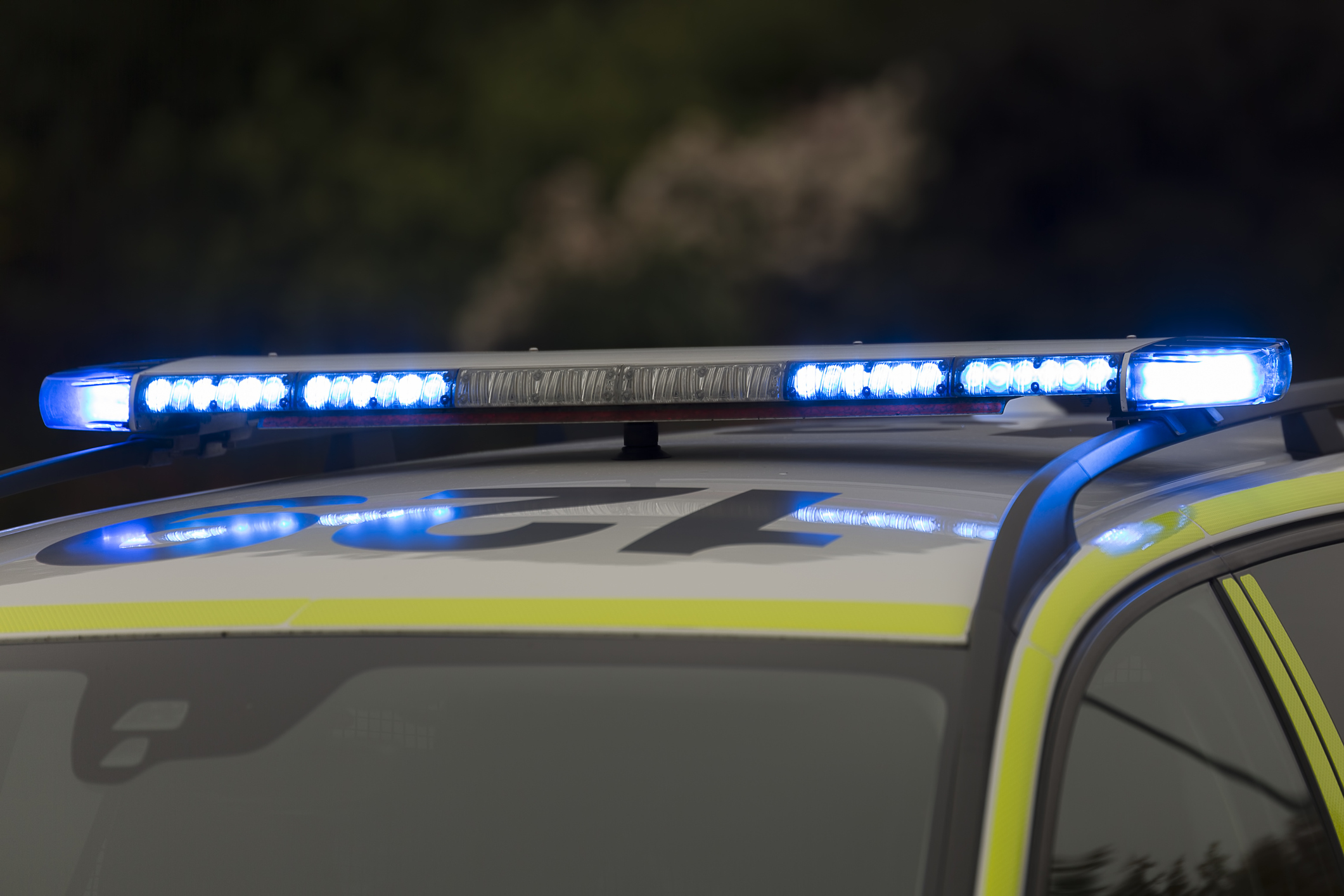 Närbild av ett polisbils tak med blå utryckningsljus som är påslagna, en del av ordet "POLICE" syns och bakgrunden är suddig.