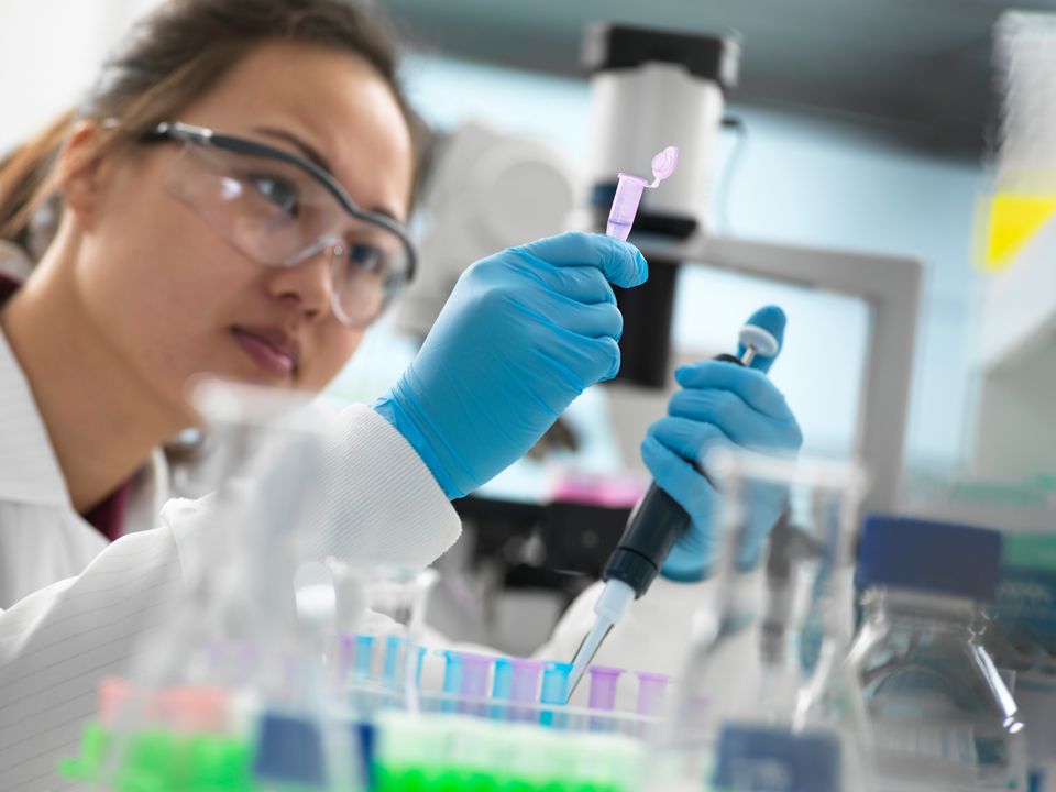 En forskare med skyddsglasögon och handskar använder en pipett för att överföra vätska till ett provrör i ett laboratorium.