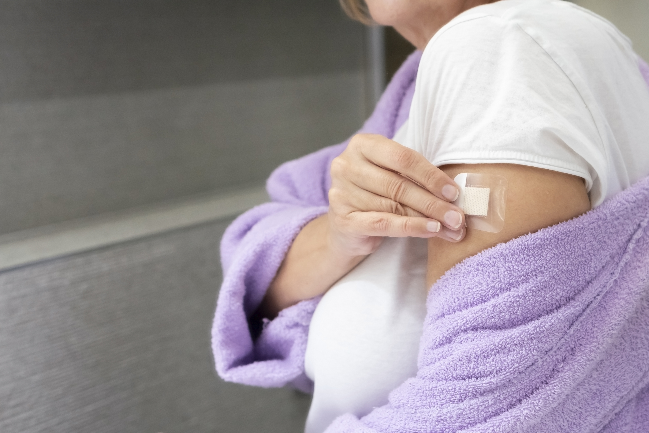 En person med vit skjorta och lila rock sätter ett plåster på överarmen, troligen efter en injektion eller vaccination.