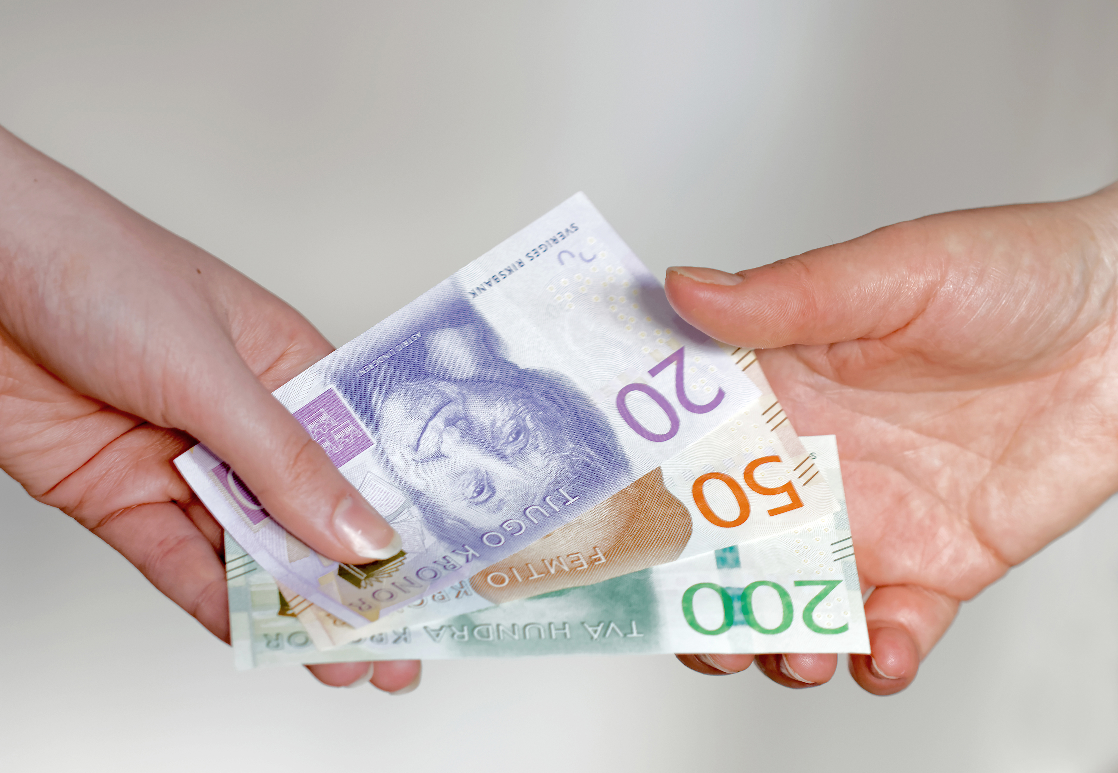En person ger svenska sedlar (20, 50 och 200 kronor) till en annan person mot en neutral bakgrund.