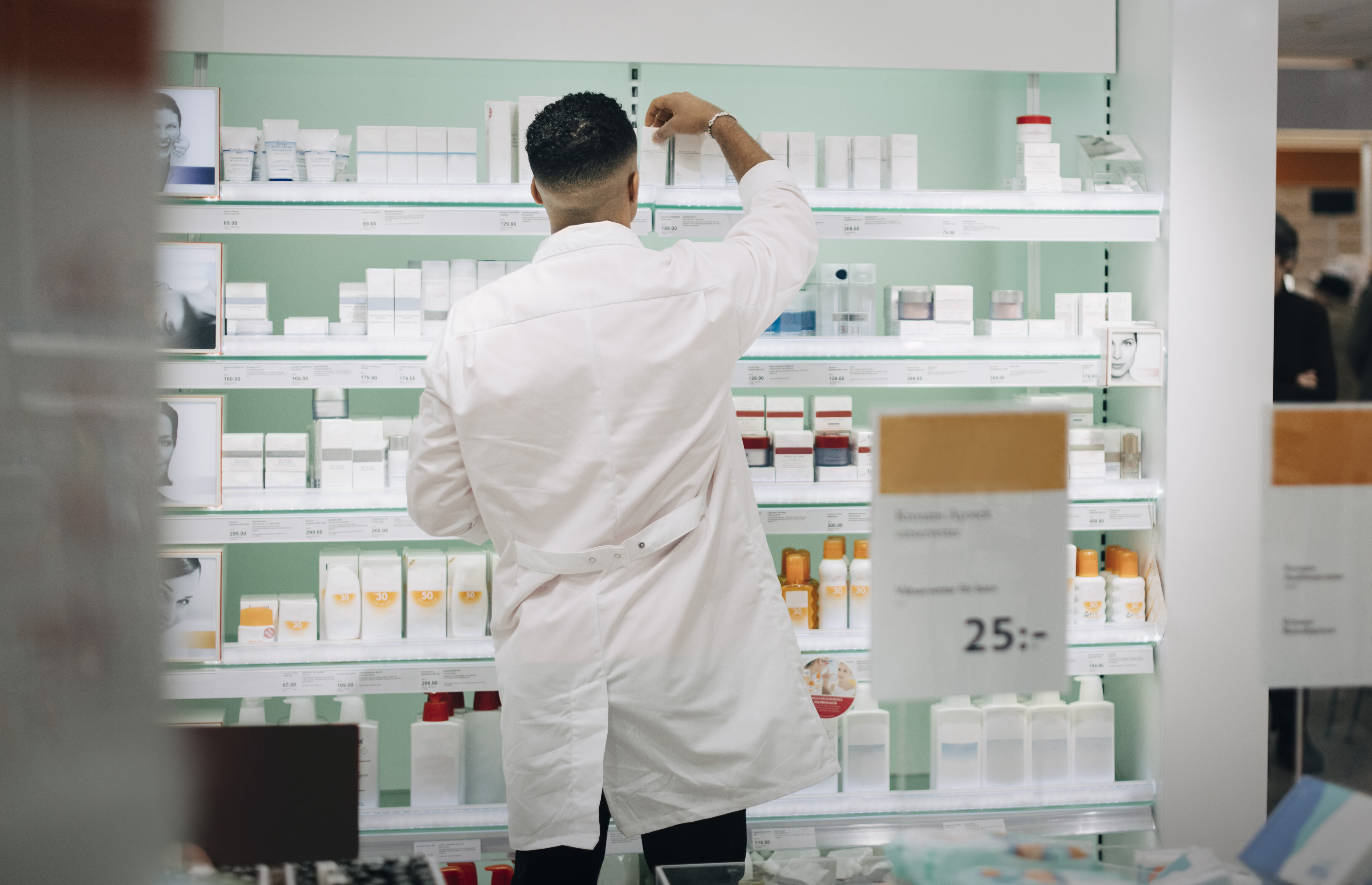 En apotekare i vit rock ordnar medicinförpackningar på hyllorna i ett apotek.