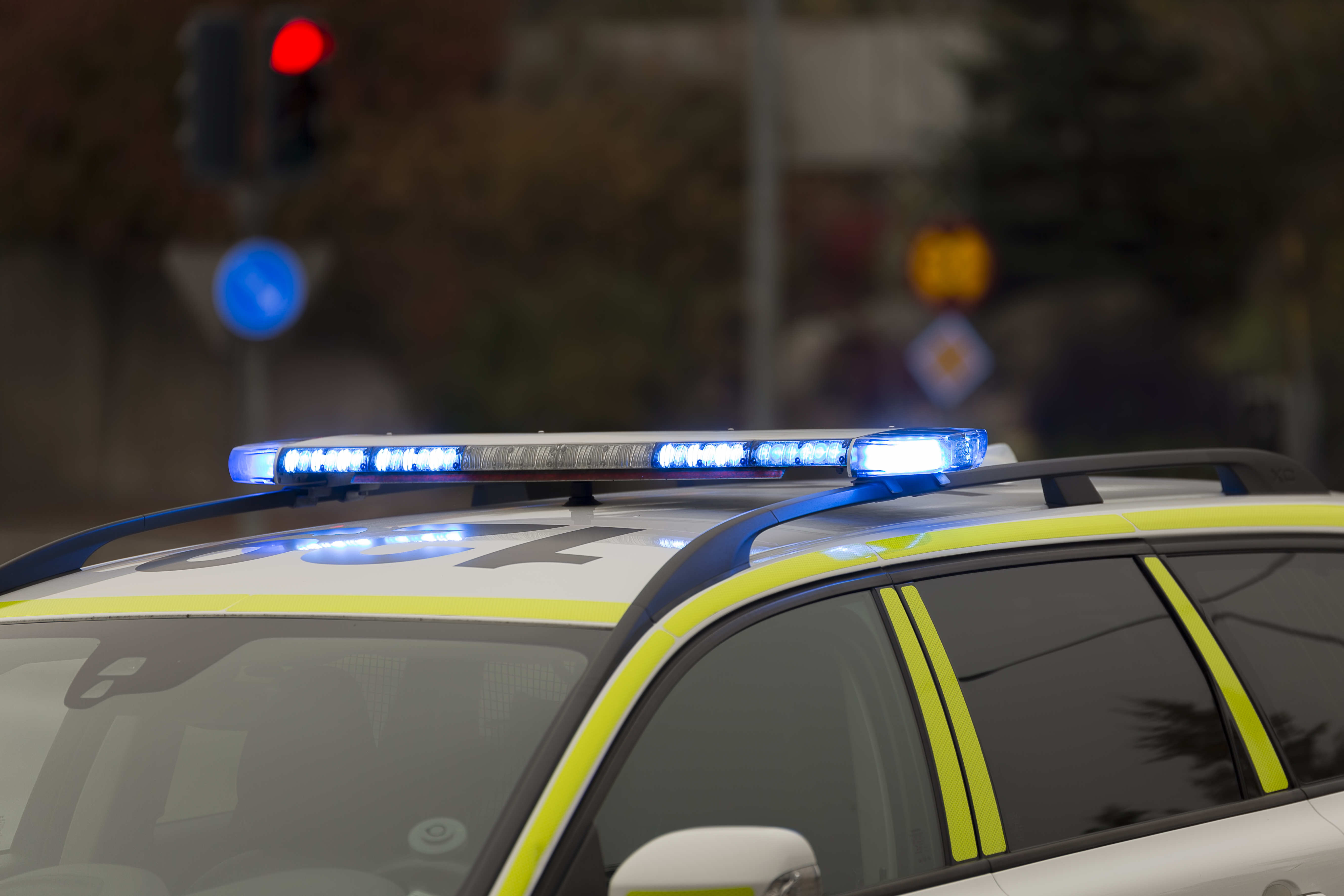 En polisbil med blåa blinkande ljus som står parkerad vid ett trafikljus på en gata i en stad.