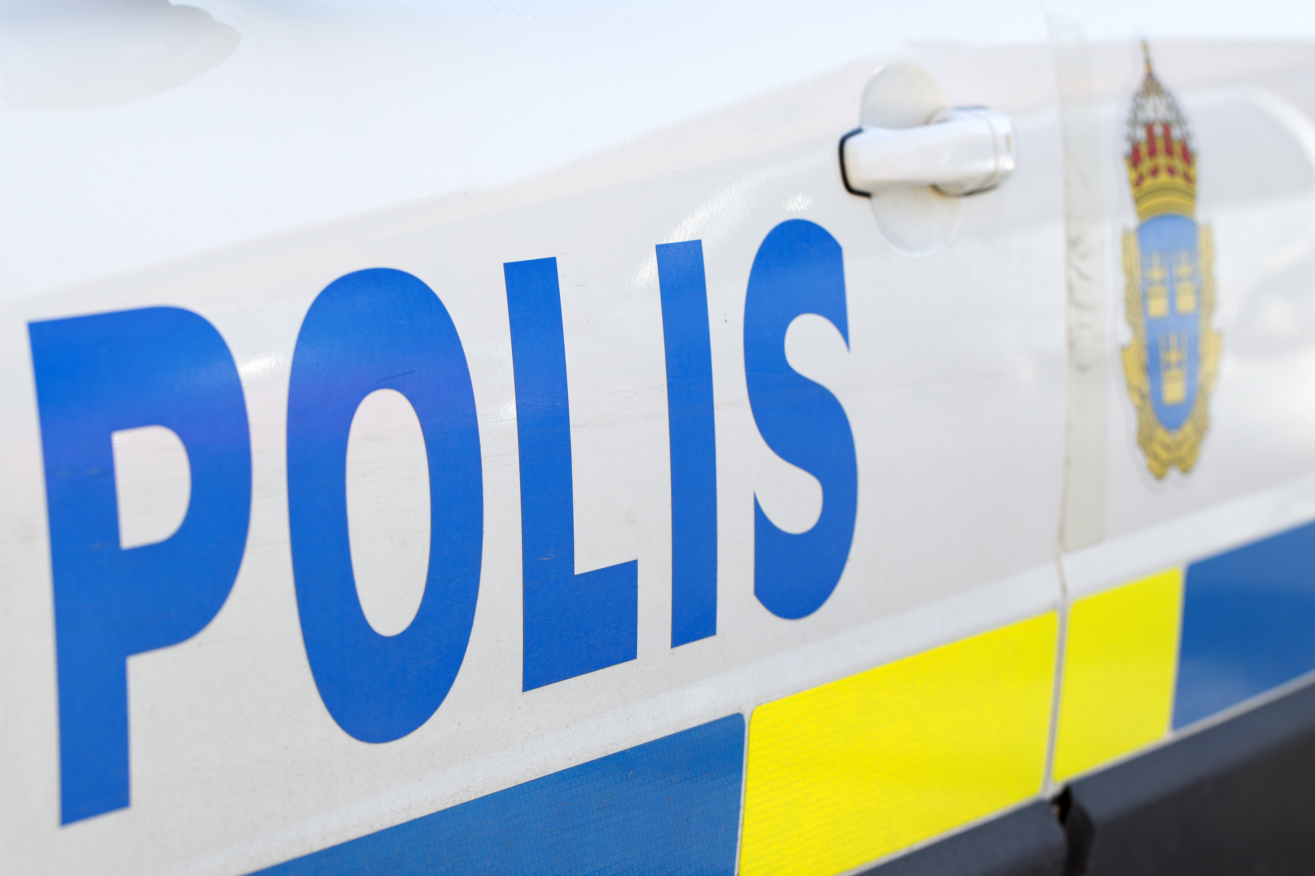 En svensk polisbil med en synlig dörr, texten ”POLIS” i blå bokstäver och det svenska polisemblemet.