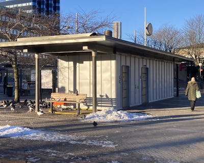 En busshållplats med bänkar och duvor i snön.