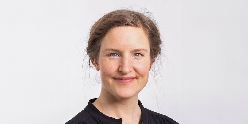 En kvinna i en svart skjorta ler mot kameran.