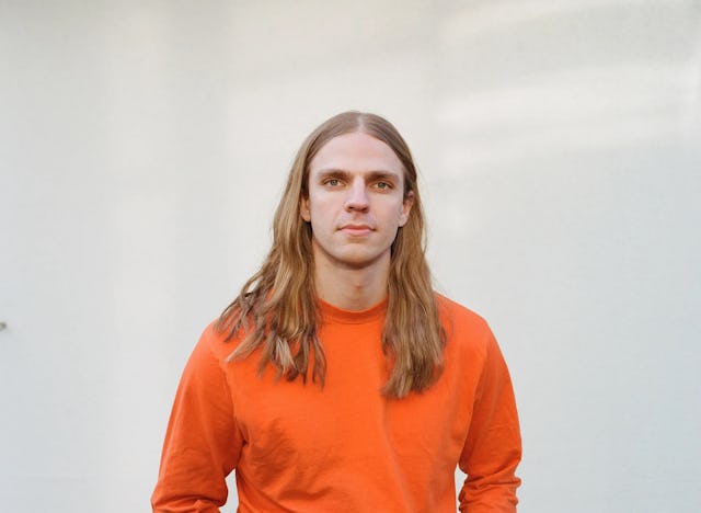 En ung man i en orange tröja och jeans.