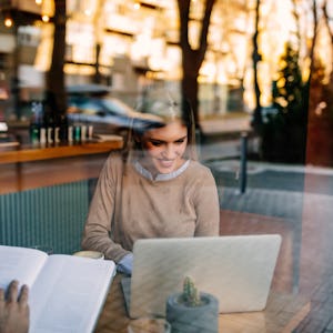 Kvinna som läser en bok och använder en bärbar dator på ett café.