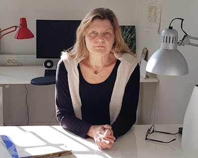 Kvinna som sitter vid ett skrivbord i ett väl upplyst rum med kontorsmaterial och en dator i bakgrunden.
