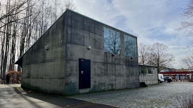 En modern betongbyggnad med stora fönster under en delvis molnig himmel.