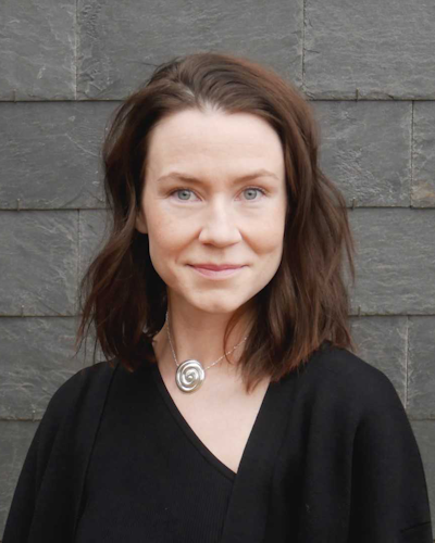 Kvinna med brunt hår och en svart topp mot en grå stenbakgrund.