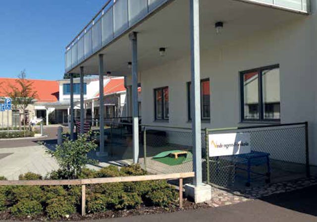 Tvåvåningsbyggnad med parkeringsplats, planterad framsida och en skylt där det står "World regions school".