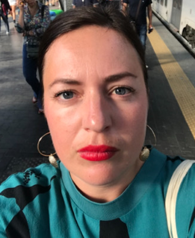 En kvinna med ett allvarligt ansiktsuttryck tar en selfie på en tågplattform.