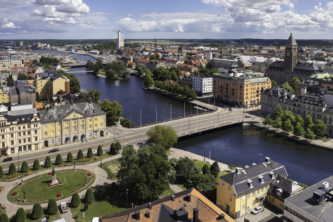 Flygvy över en stad med en flod, broar samt en blandning av historiska och moderna byggnader under molnig himmel.